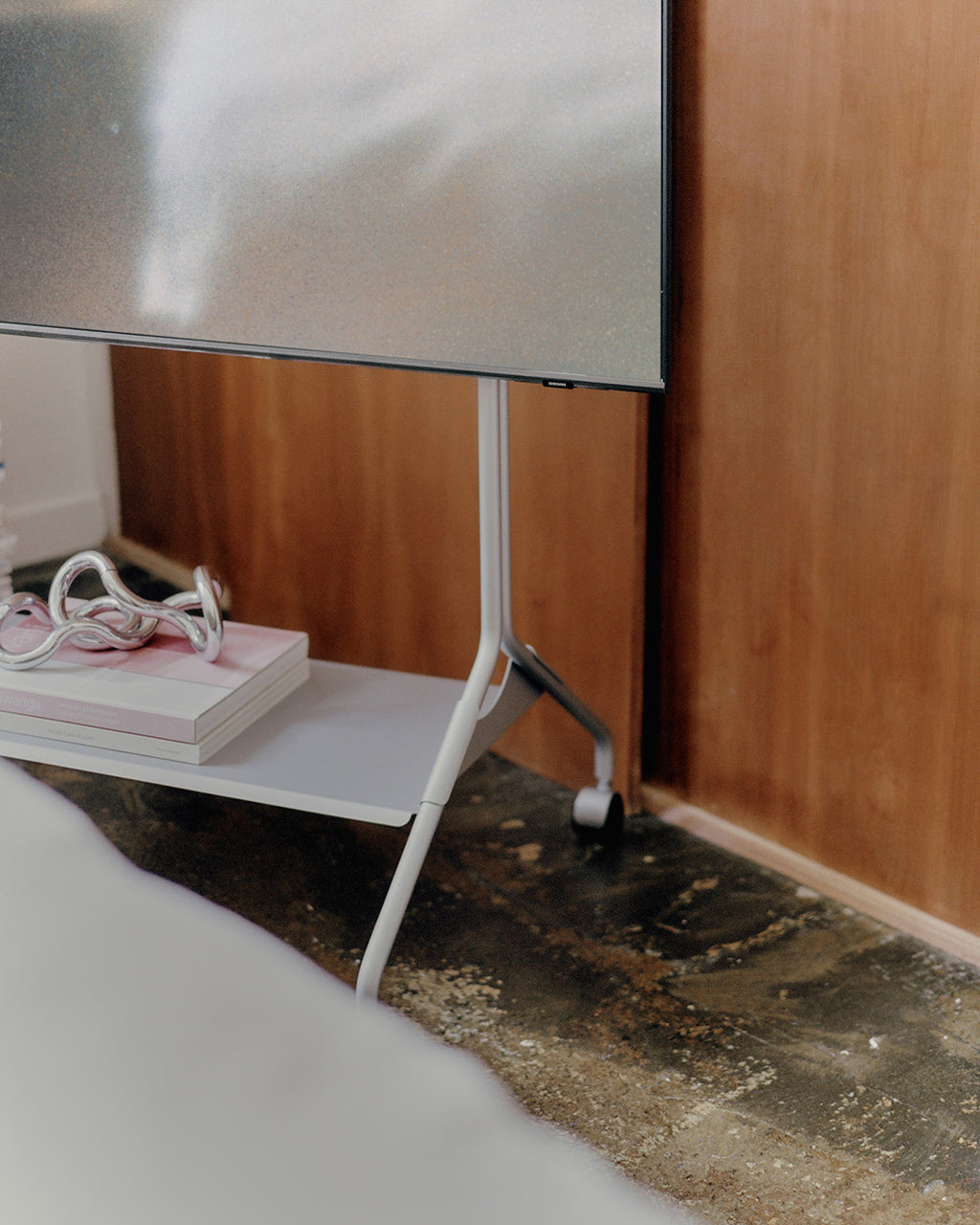 Moon in Cloudy Silver TV stand with wheels in a wood-paneled room, close-up on shelf with books and decor